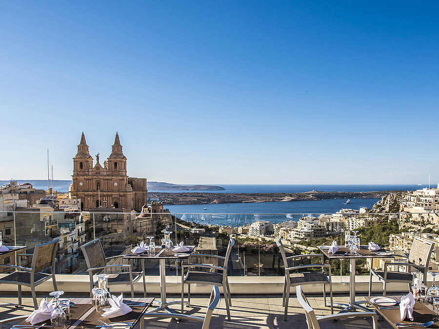 Panoramaterrasse des Restaurants Antonine Al Fresco im Maritim Antonine Hotel & Spa Malta mit Blick auf die Kirche von Mellieħa und die Bucht.