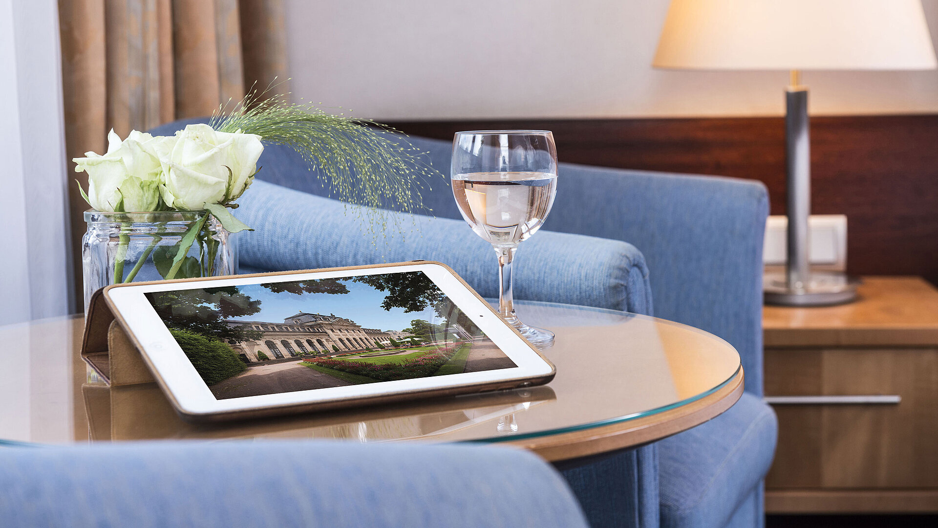 Gemütlicher Sitzbereich im Maritim Hotel Fulda mit Tablet, Glas Wasser und weißen Rosen auf einem Glastisch.