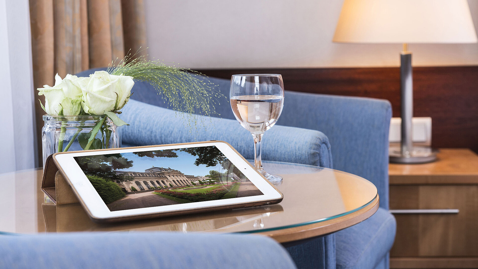 Cozy seating area at Maritim Hotel Fulda with tablet, glass of water, and white roses on a glass table.