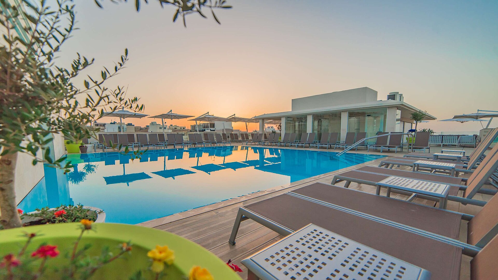 Outdoor pool with sun loungers and parasols during atmospheric sunset